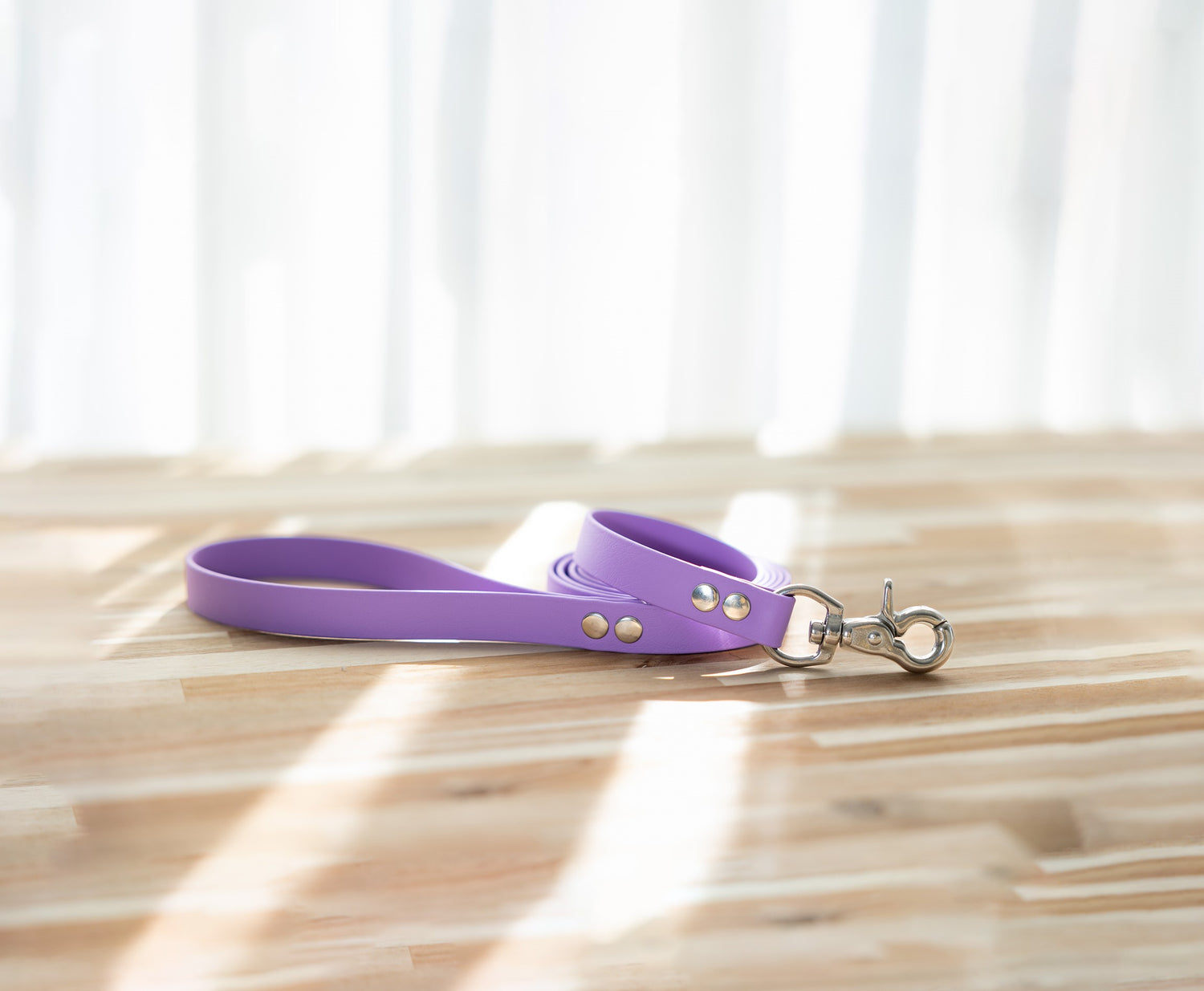 Amethyst Biothane dog lead laid out on a light wooden floor, featuring a metal clasp on one end and a flat strap design.
